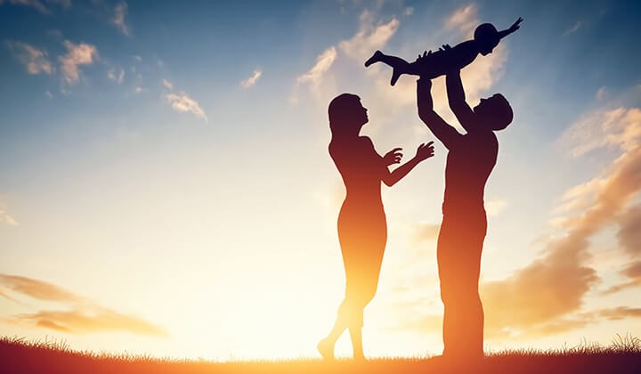 Vater hält Baby hoch Zum Sonnenschutz für Kinder zählt auch Kleidung