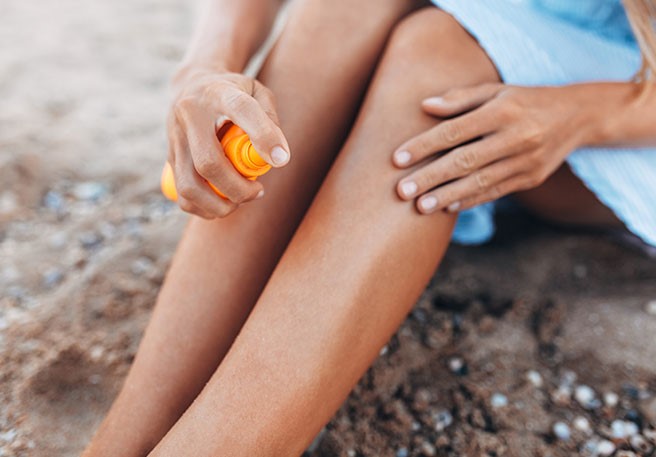 Frau sprüht Sonnenspray auf Frau am Strand mit Sonnenschutz Spray
