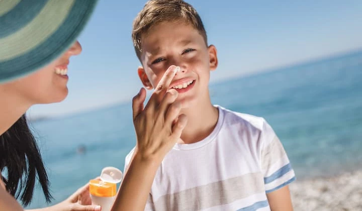 Sonnencreme schützt Kinder vor Sonnenbrand Frau cremt Jungen im Gesicht mit Sonnencreme ein